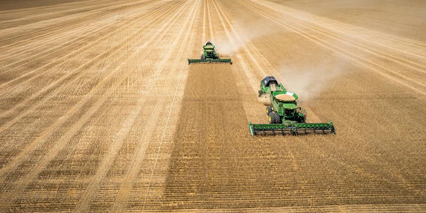 The image shows two large farming machines harvesting crops in a vast field