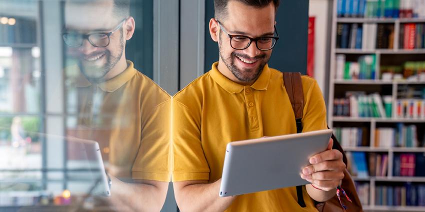 The image shows a smiling man in a library or bookstore reading on a tablet